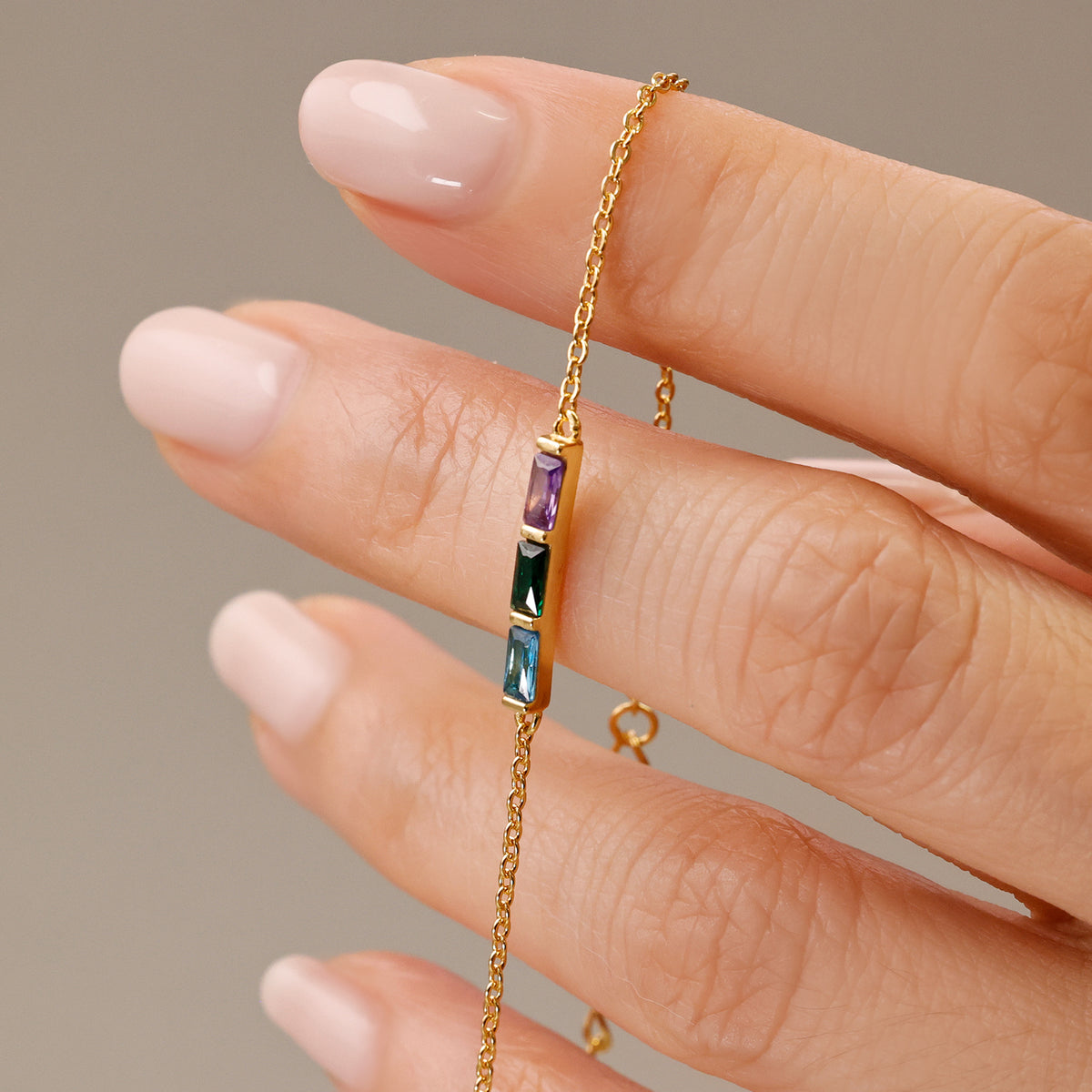 Personalisiertes Geburtsstein-Armband in Gold mit drei Steinen zwischen den Fingern gehalten