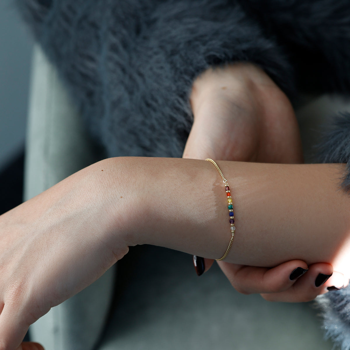 Frau trägt Chakra Armband in Gold am Handgelenk, im Hintergrund graue Felljacke