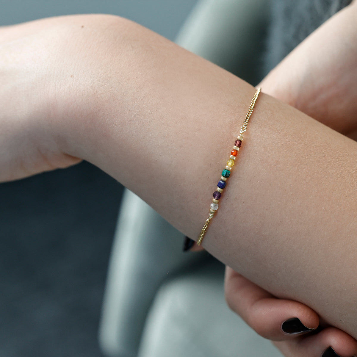 Frau trägt Chakra Armband in Gold am Handgelenk, Nahaufnahme mit schwarzem Nagellack