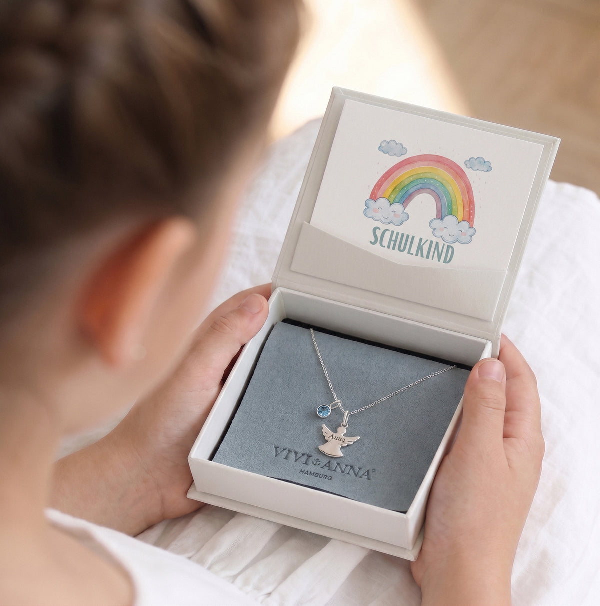 Kind hält Geschenkbox zur Einschulung mit Schulkind-Karte und silberner Schutzengel-Kette