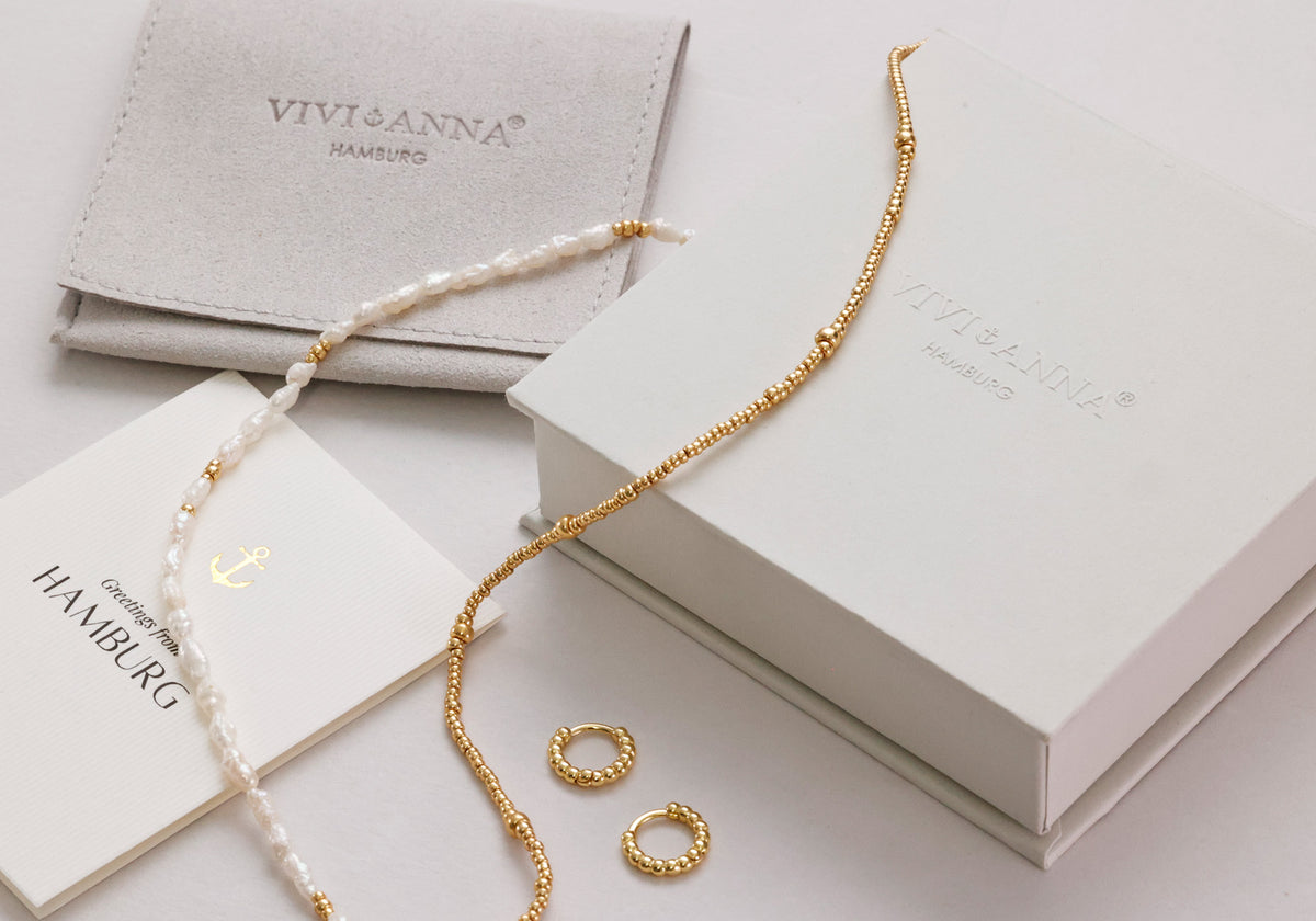Geschenkverpackung mit Schmuckbeutel, Grußkarte, Perlenkette und goldenen Creolen