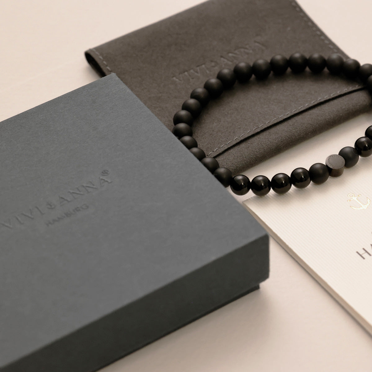 Herren-Geschenkverpackung in Grau mit Etui und Armband aus mattschwarzen Steinperlen