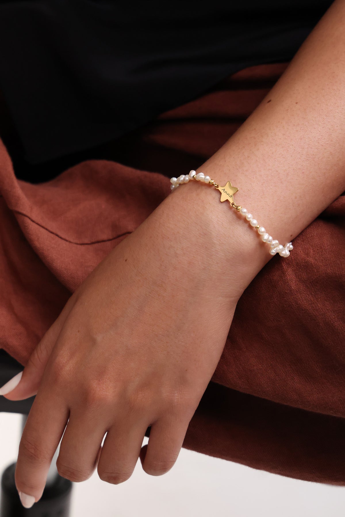 Frau trägt Süßwasserperlen Armband mit goldenem Sternanhänger, sitzend am Handgelenk