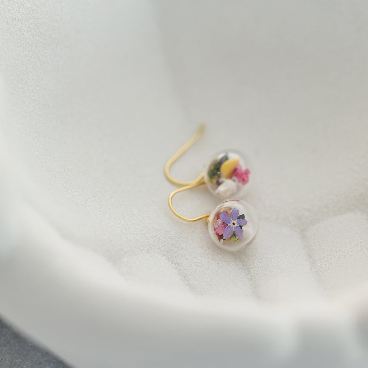 Echte-Blumen-Ohrringe liegend in weißer Schale mit bunten Trockenblüten