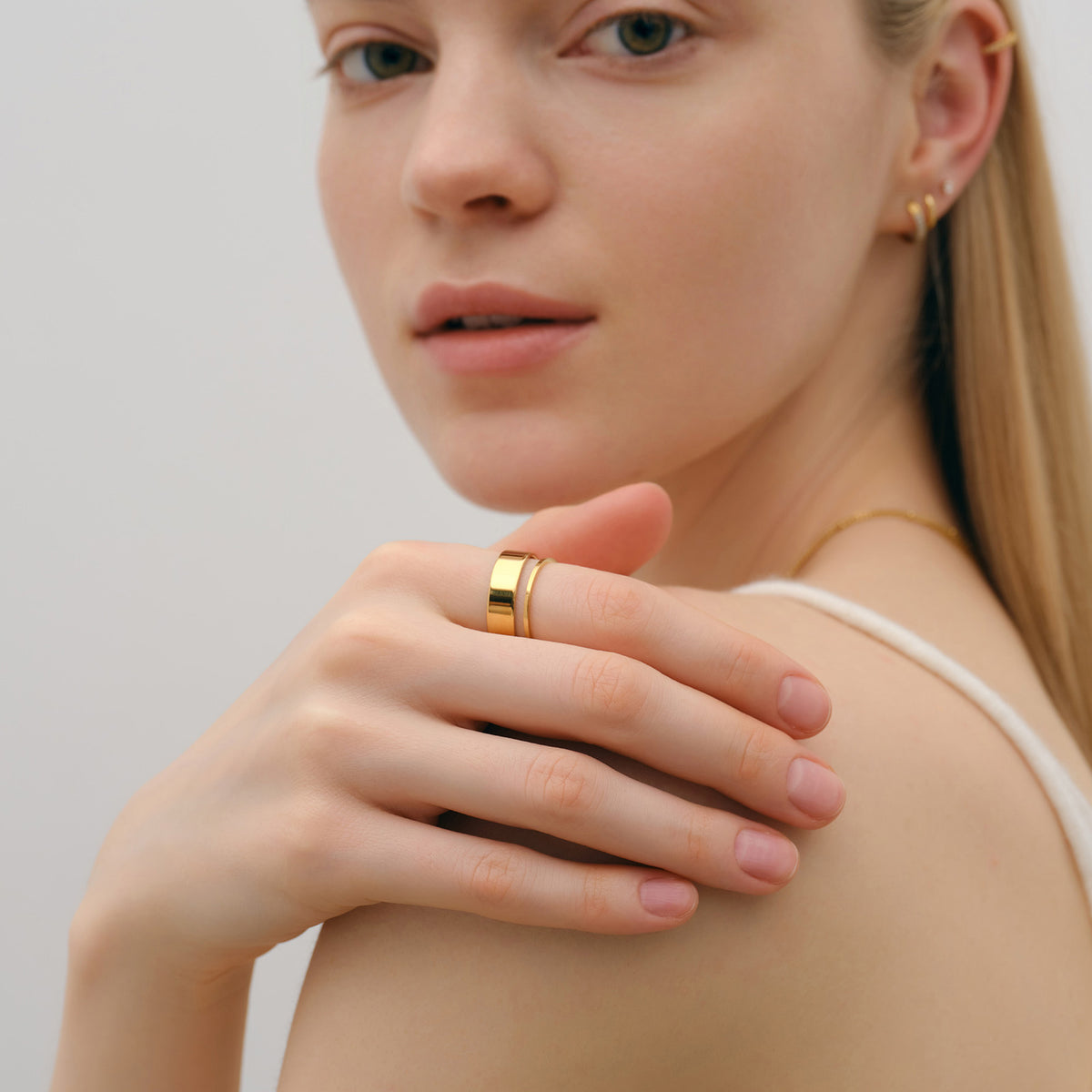 Feiner Stapelring in Gold – Frau trägt Ringe am Finger, Hand an der Schulter