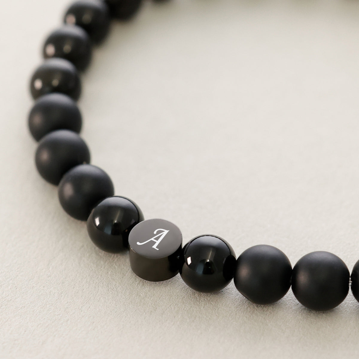 Armband mit Obsidian- und Onyx-Perlen, silbernes Plättchen mit Initiale 'A' im Detail