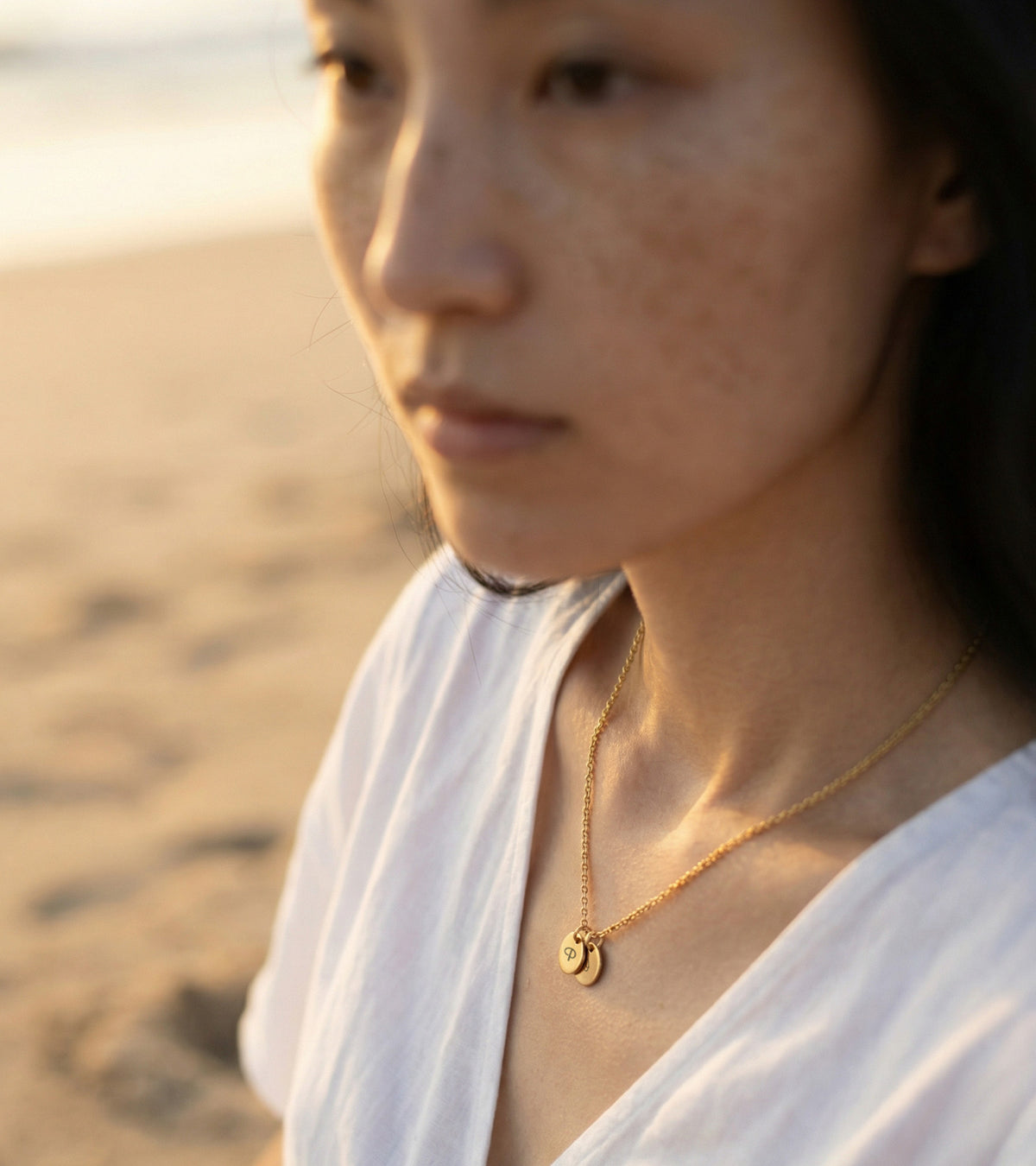 Personalisierte Kette mit rundem Plättchen wasserfest in Gold – Frau trägt Kette am Strand, Nahaufnahme im Profil