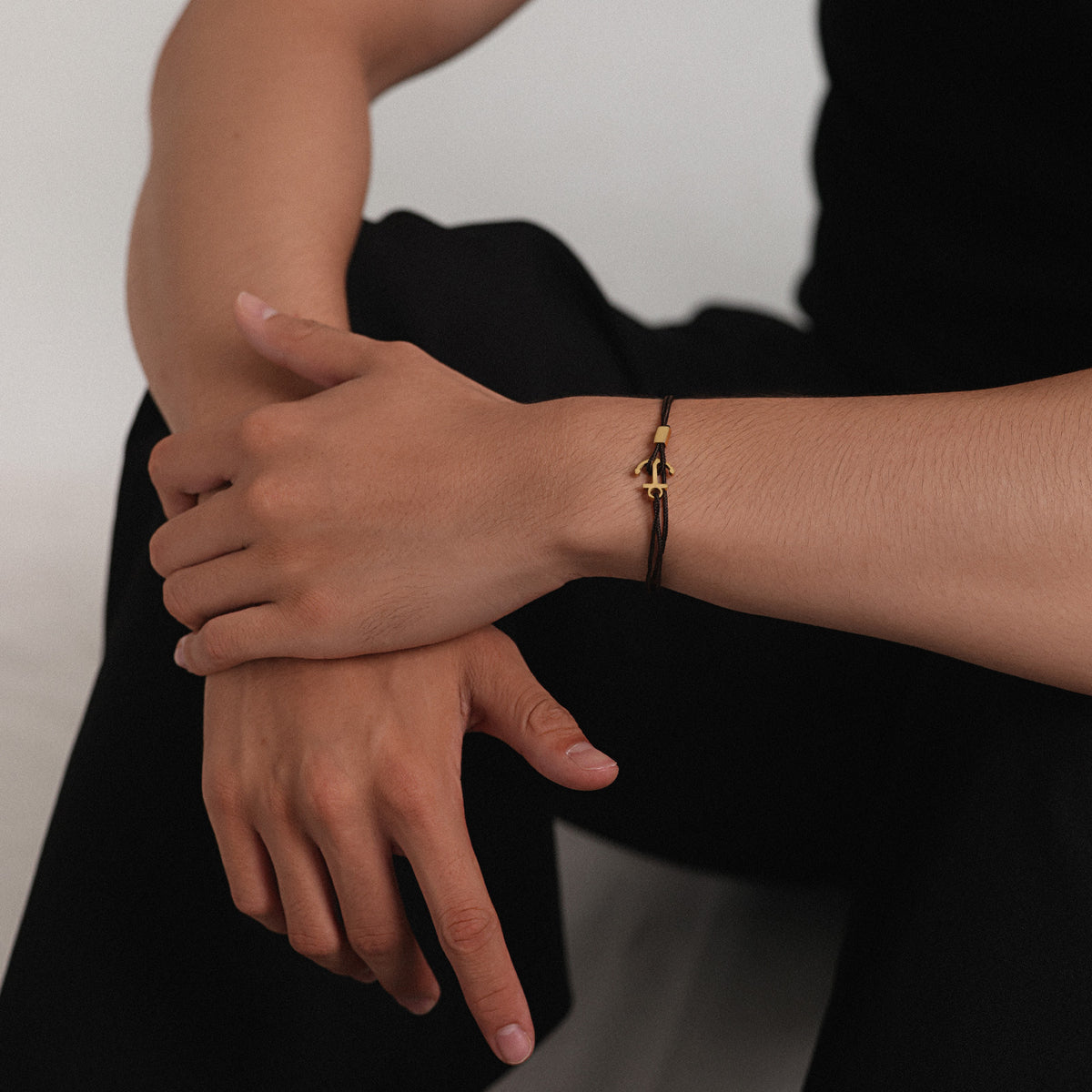 Mann trägt braunes Unisex Armband mit Gravur & Ankerhaken am Handgelenk, Arme verschränkt