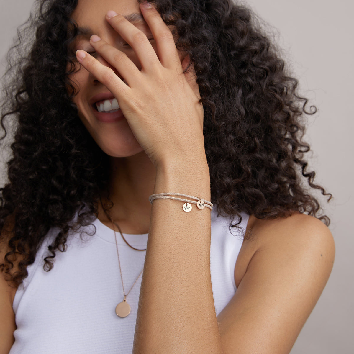 Frau trägt Segeltau Armband in Beige mit rundem Anhänger, lachend mit Hand vorm Gesicht