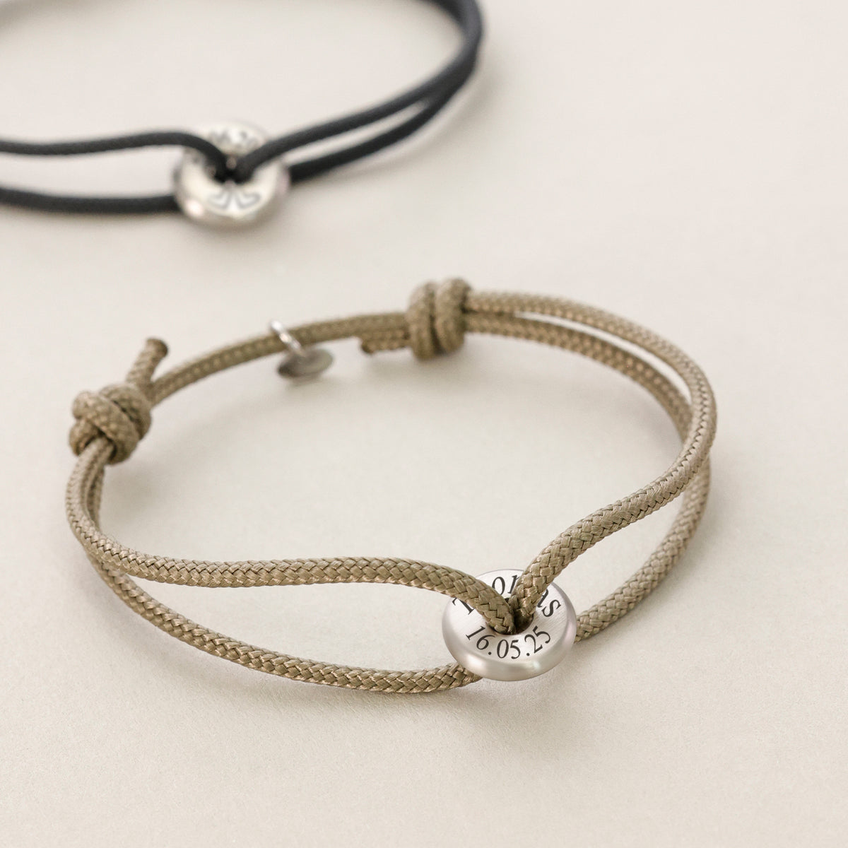 Zwei geknotete Textilarmbänder in Schwarz und Beige mit gravierter Silberperle und Datum
