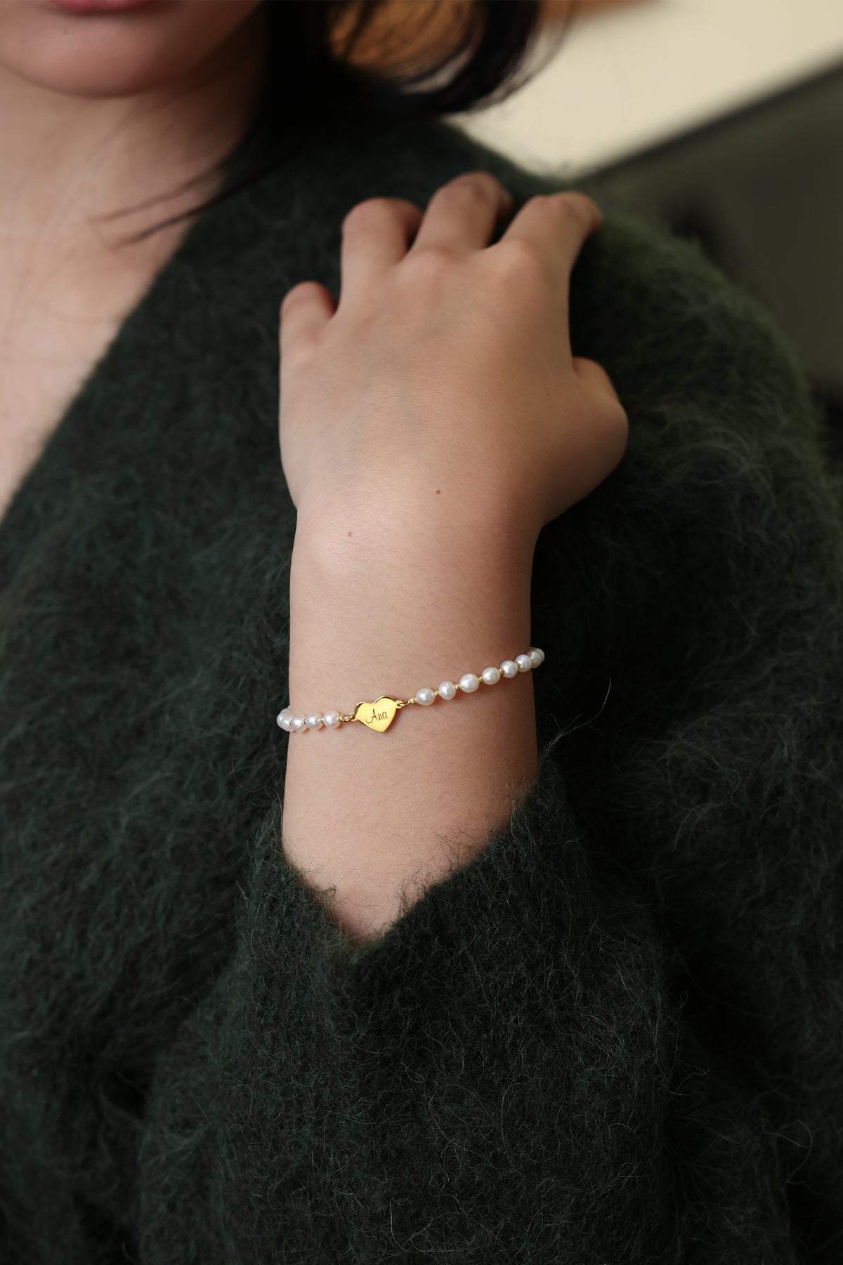 Frau trägt Süßwasser-Perlenarmband mit goldenem Herz-Anhänger am Handgelenk, Nahaufnahme