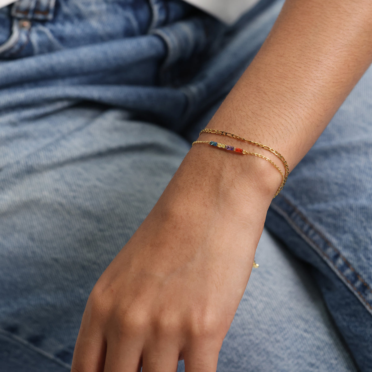 Personalisiertes Geburtsstein-Armband in Gold am Handgelenk vor Jeans-Hintergrund
