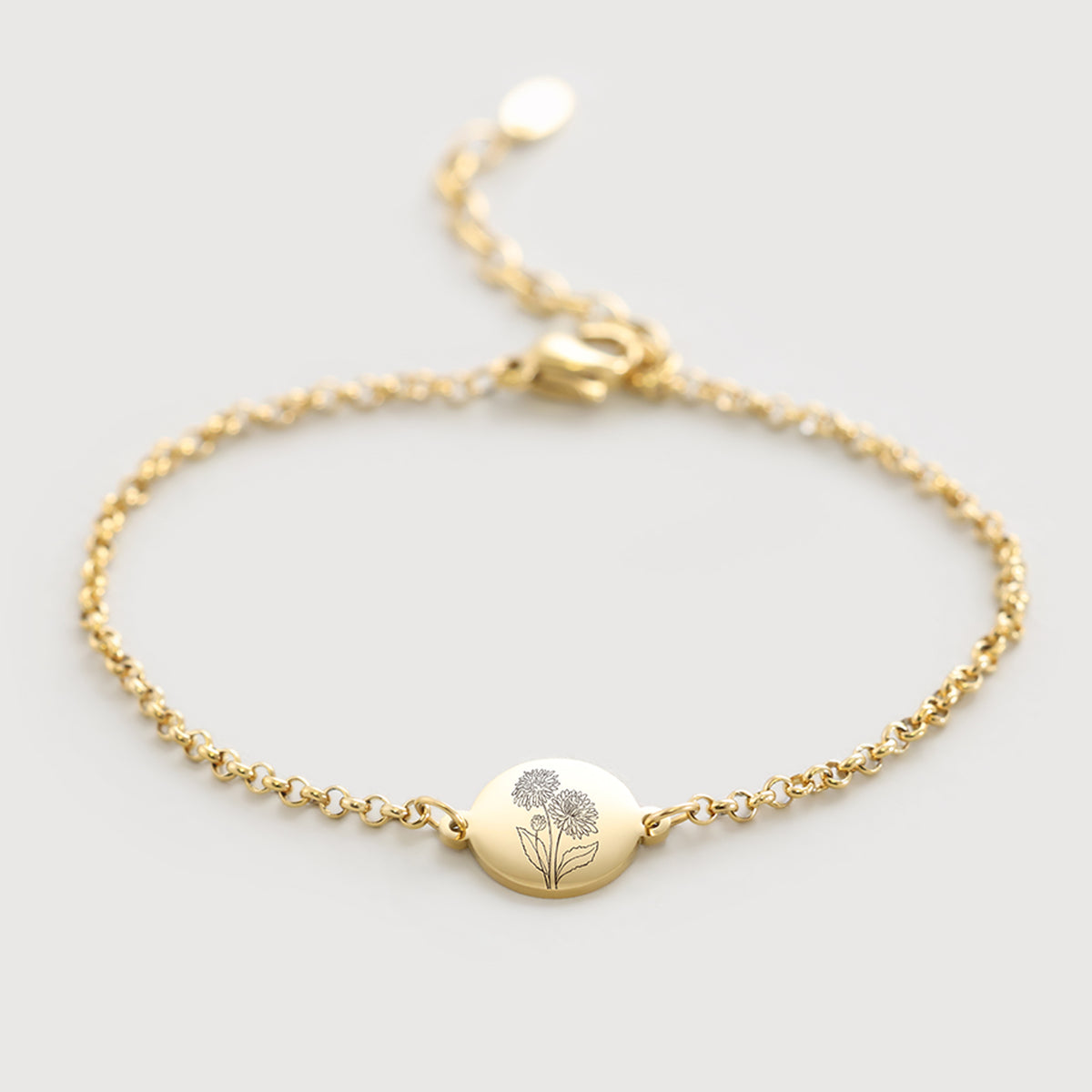 Geburtsblumen-Armband mit rundem Plättchen in Gold, flach liegend mit Blumengravur