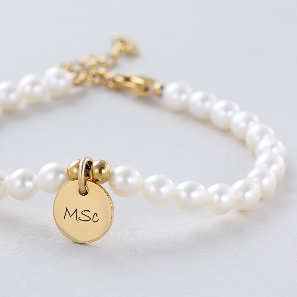 Nahaufnahme des goldenen Gravurplättchens mit Initialen am Süßwasserperlen-Armband