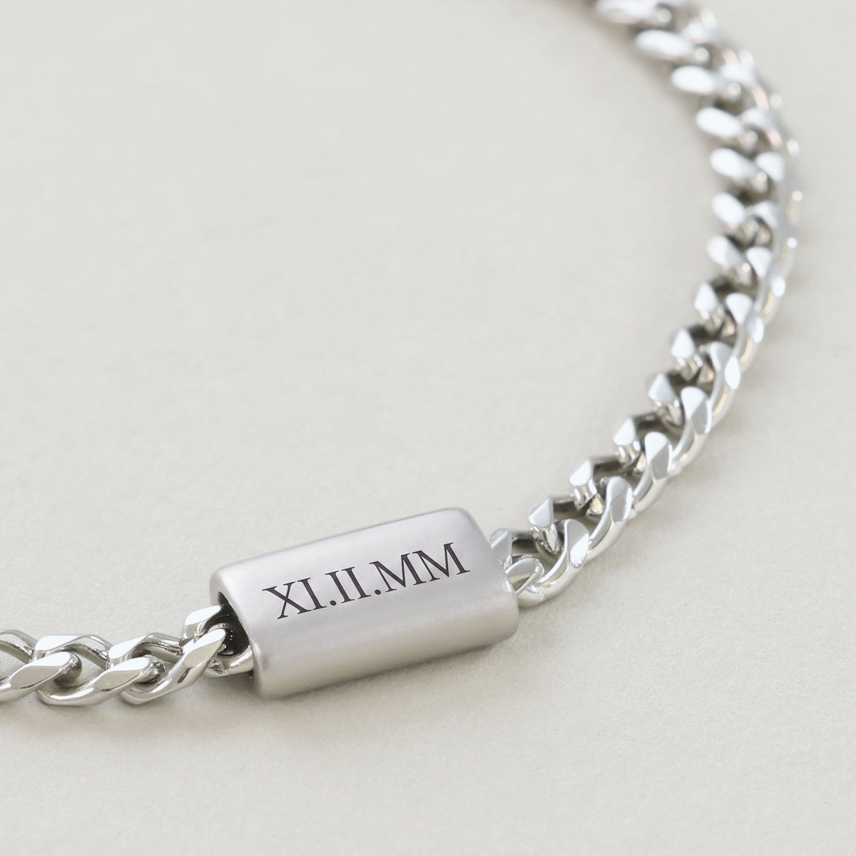 Nahaufnahme: graviertes Plättchen mit römischen Ziffern 'XI.II.MM' am Cuban-Armband