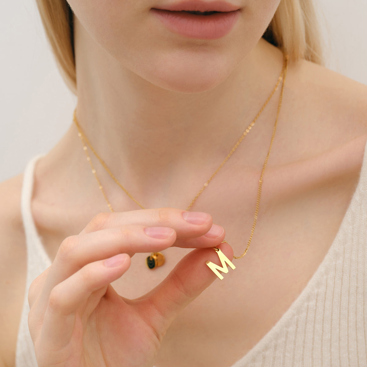 Frau trägt goldene Kette mit Buchstaben-Anhänger M in der Hand