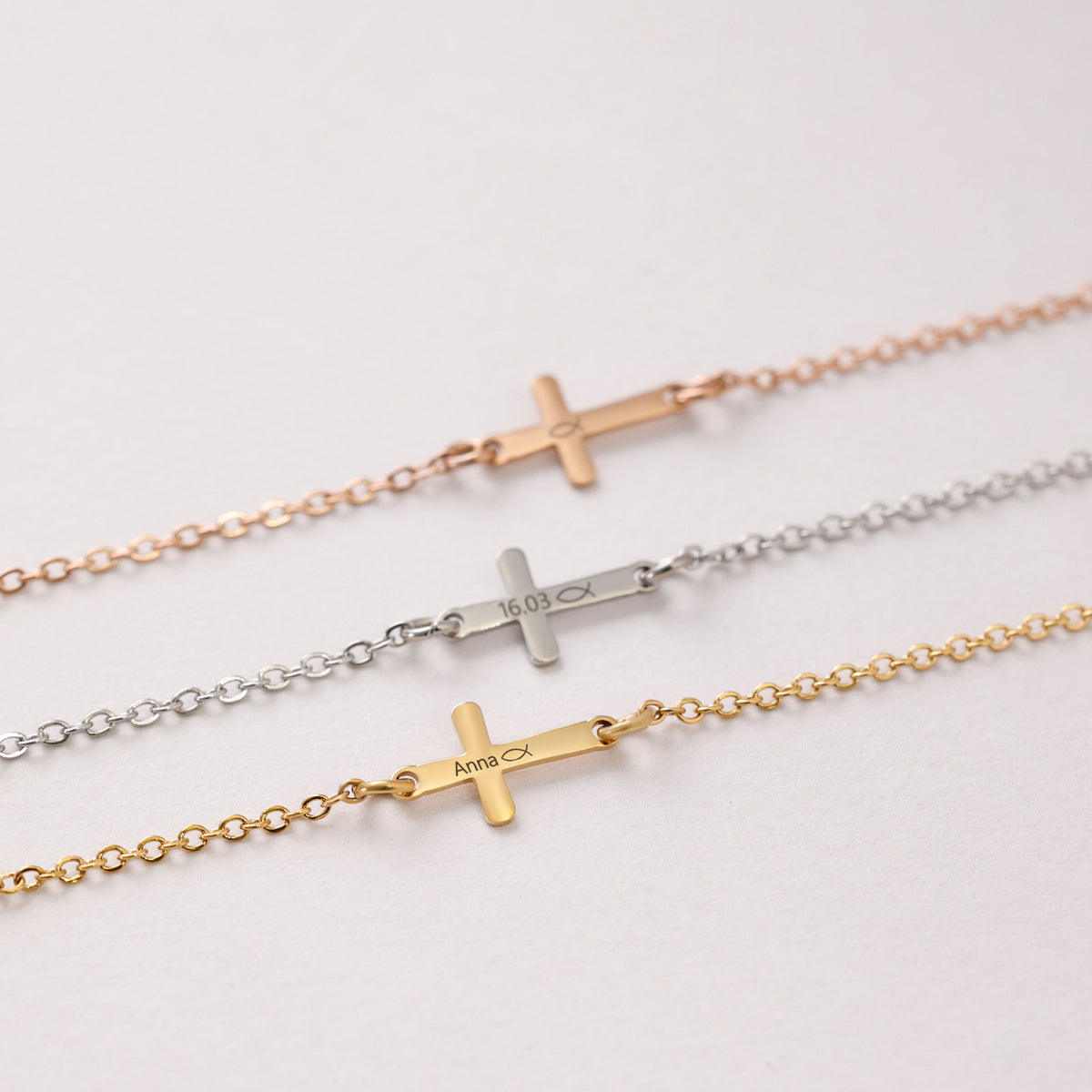 Drei Kreuz-Armbänder im Vergleich – Roségold, Silber und Gold, jeweils graviert mit Namen oder Datum