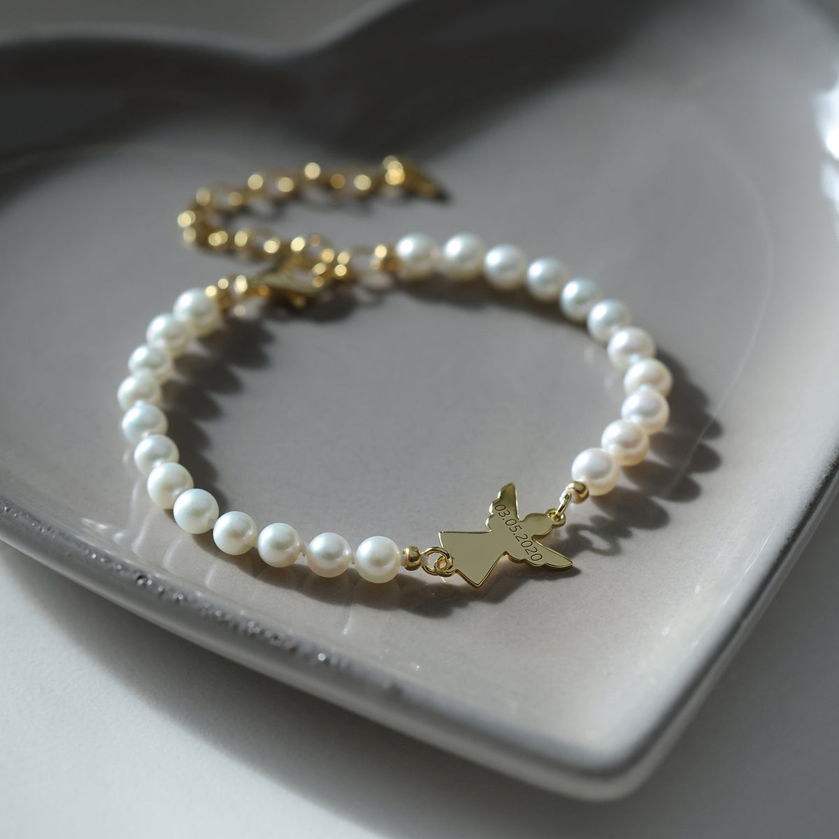 Perlenarmband mit goldenem Schutzengel auf grauer Keramikschale mit Verlängerungskette