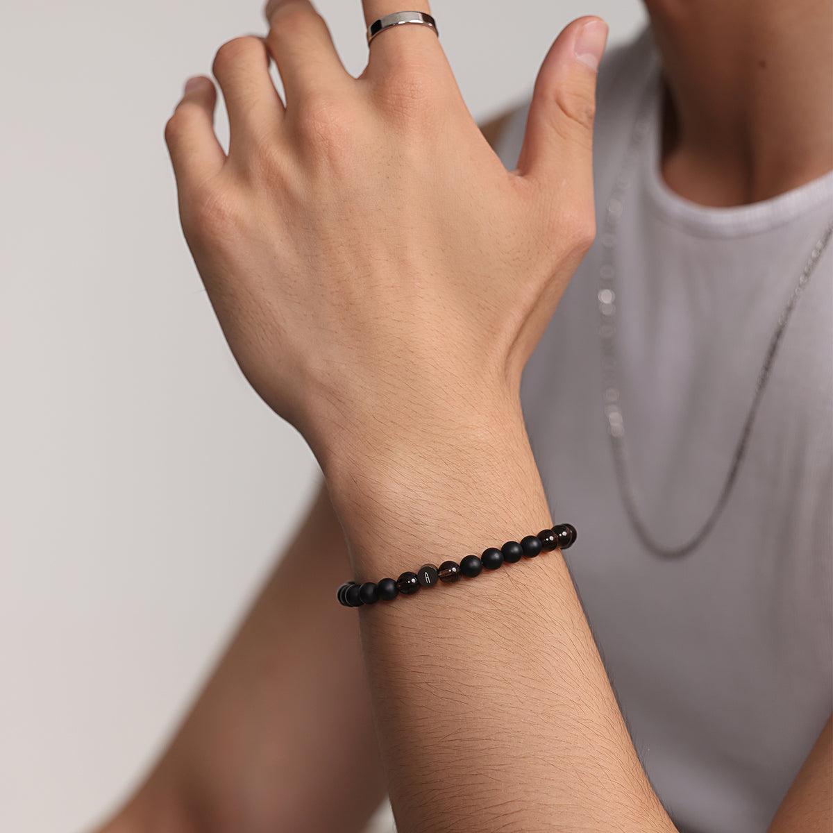 Mann trägt Naturstein-Armband aus Rauchquarz und Onyx am Handgelenk, mit Ring und Halskette