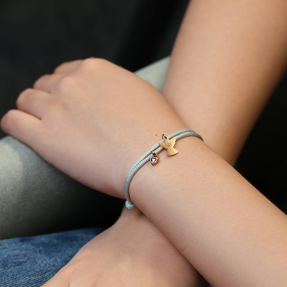 Person trägt graues Segeltau Armband mit goldenem Schutzengel-Anhänger am Handgelenk
