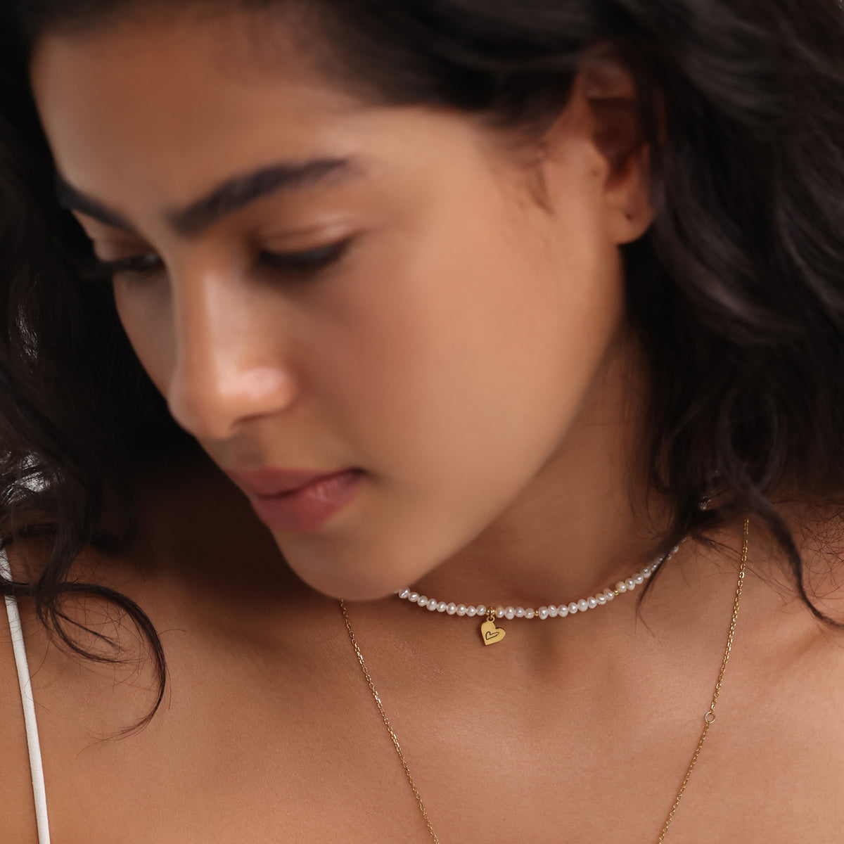 Frau trägt Perlenkette mit Herzanhänger als Choker, kombiniert mit zweiter Goldkette