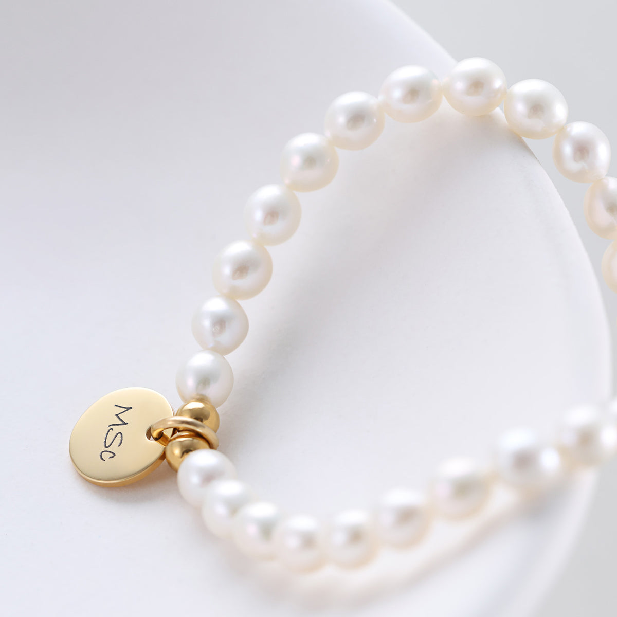 Perlenarmband mit goldenem Gravurplättchen, Detailansicht auf weißem Untergrund