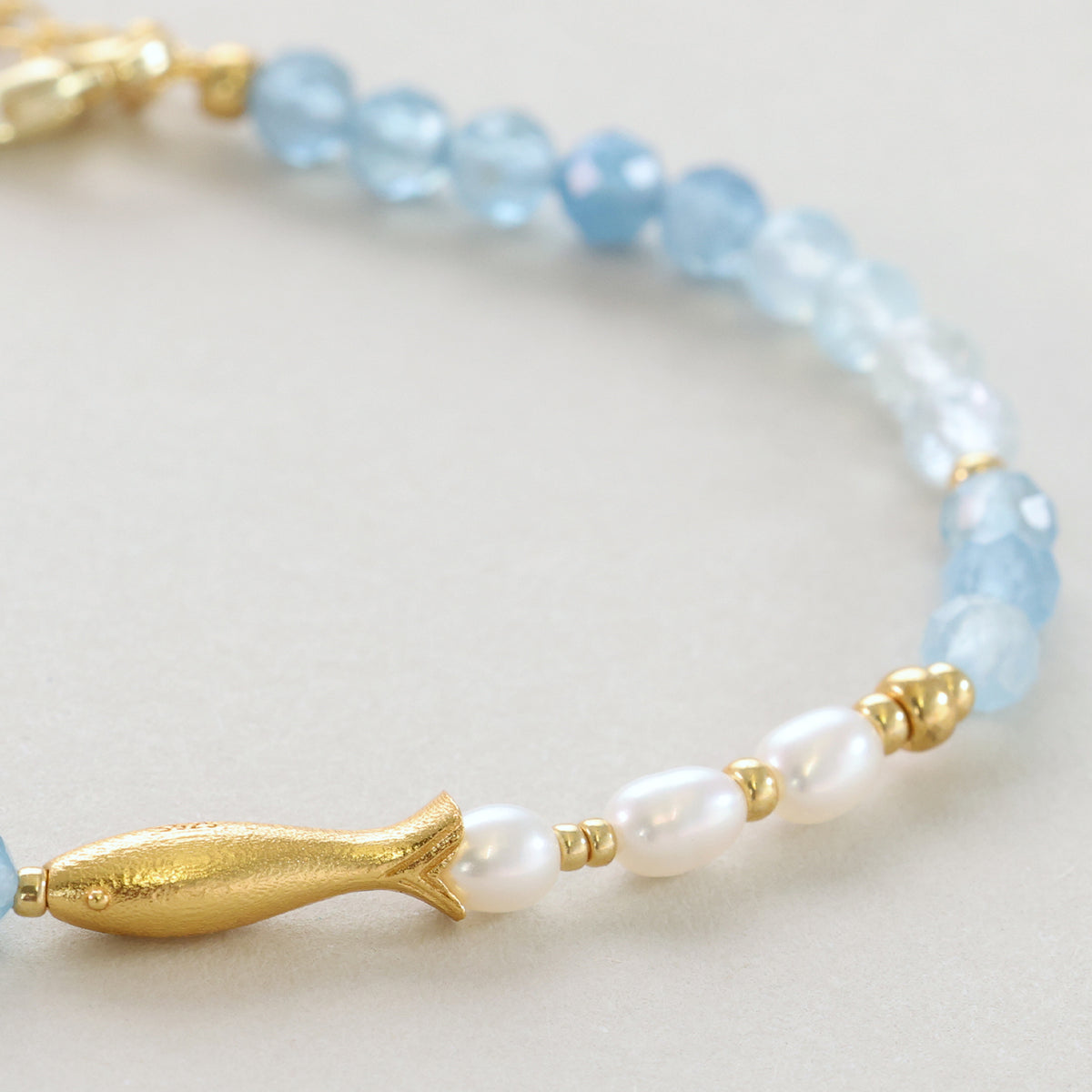 Goldener Fisch-Anhänger des Armbands zwischen Süßwasserperlen und Aquamarin-Perlen
