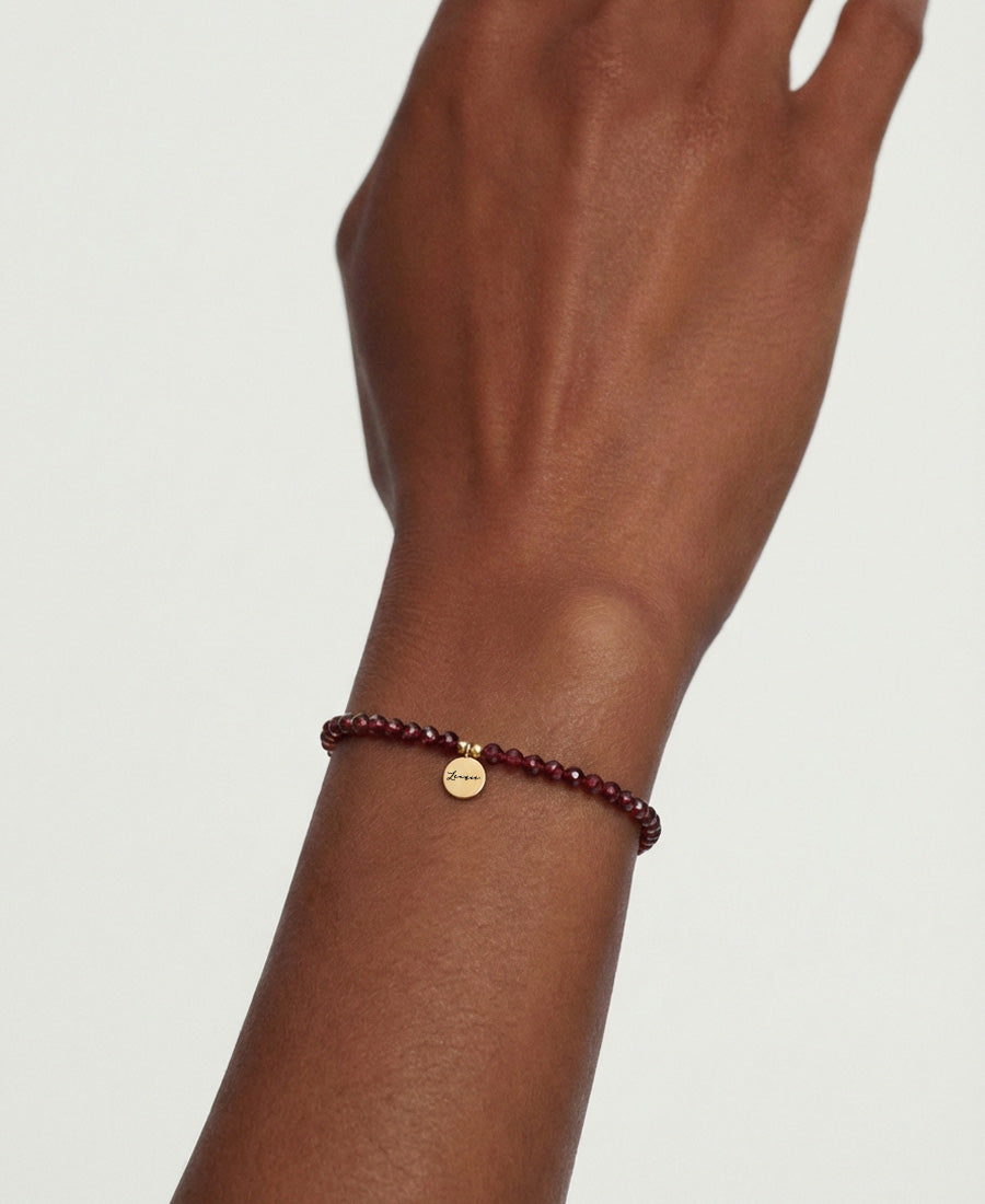 Frau trägt Granat-Armband mit rotem Perlenbesatz und Gravuranhänger am Handgelenk