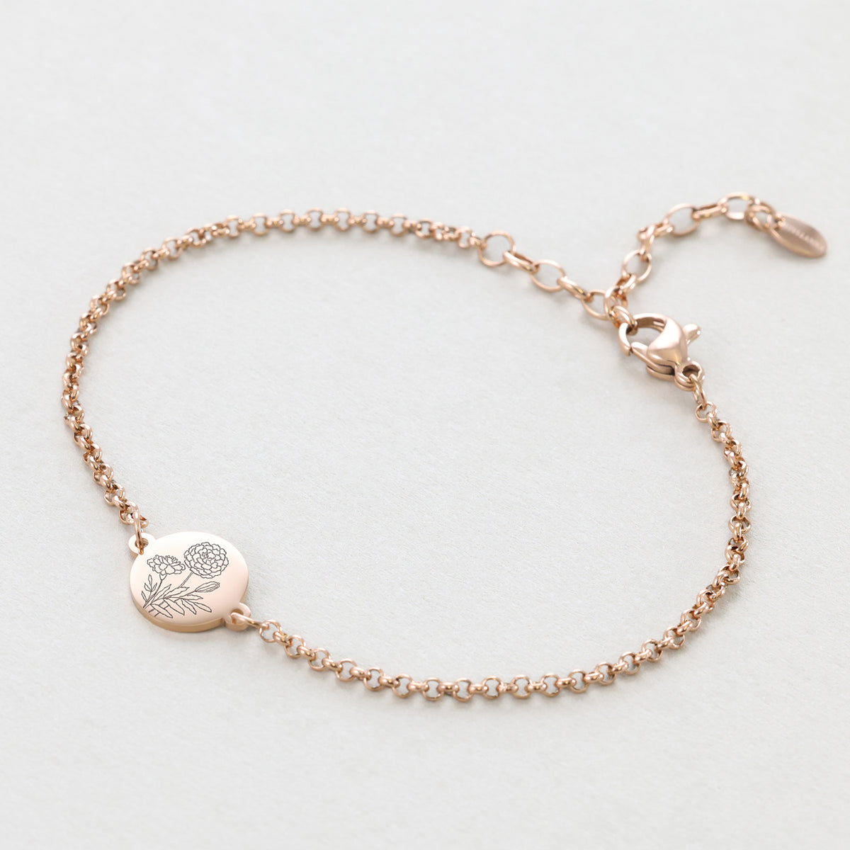 Geburtsblumen-Armband mit rundem Plättchen in Roségold, flach liegend mit Blumengravur