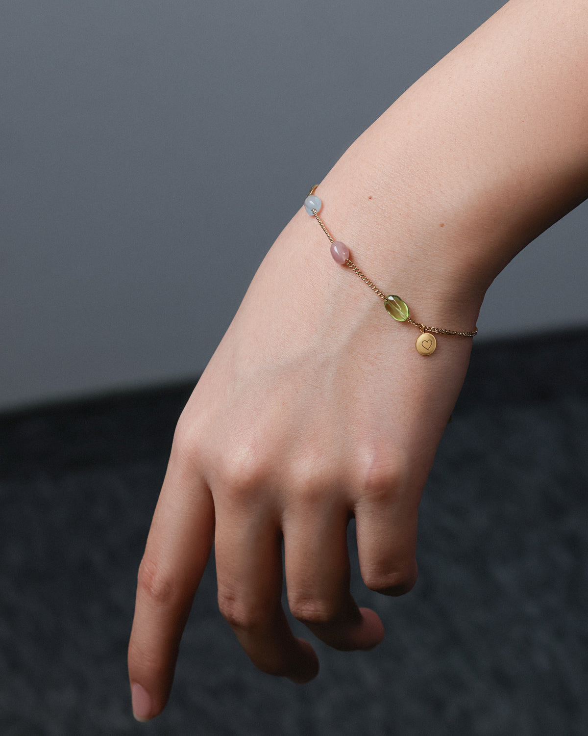 Naturstein-Armband am Handgelenk mit Farbsteinen und kleinem Herz-Anhänger