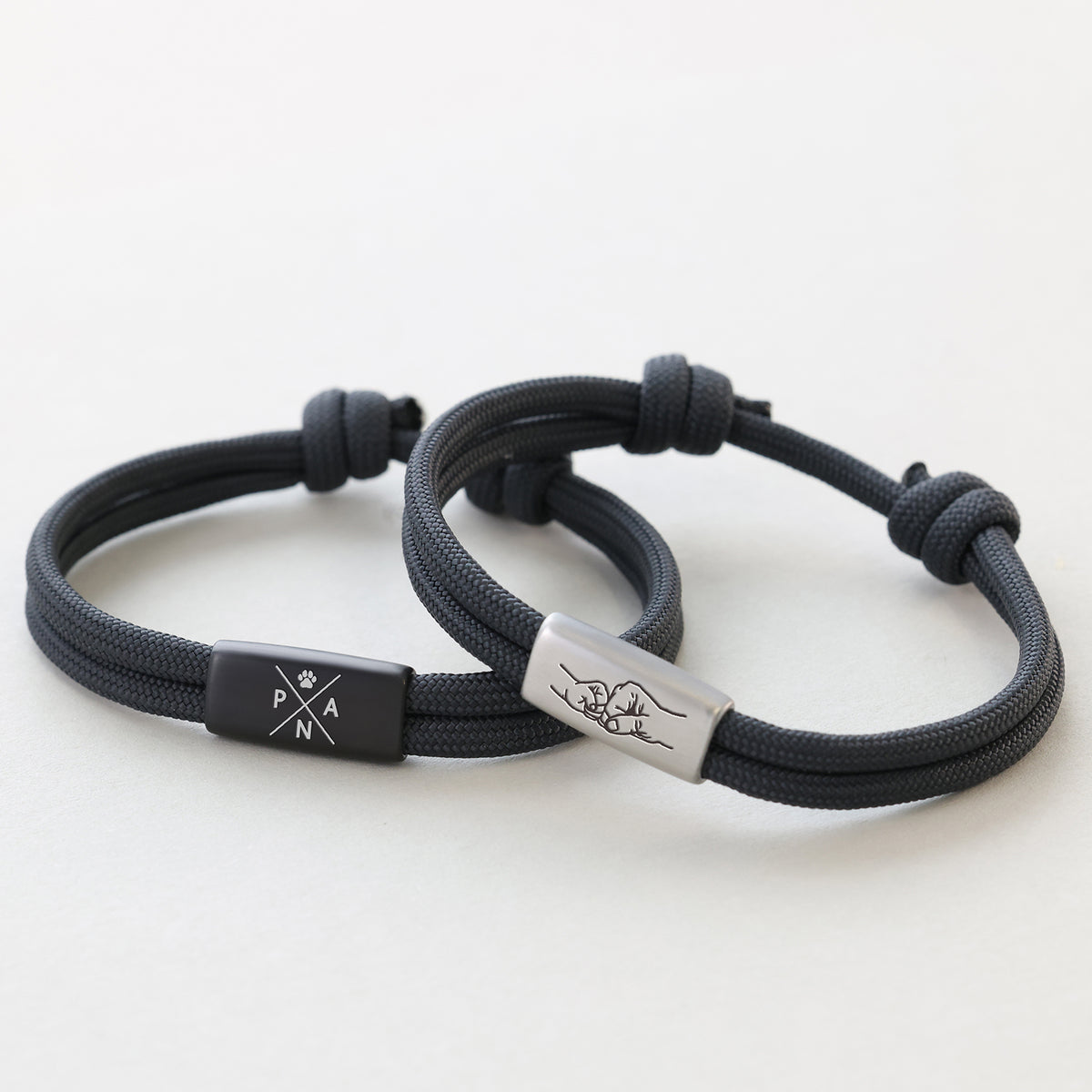 Zwei personalisierte Segeltau Armbänder in Anthrazit – Kompass mit Pfotenabdruck und Faustgruß-Symbol graviert