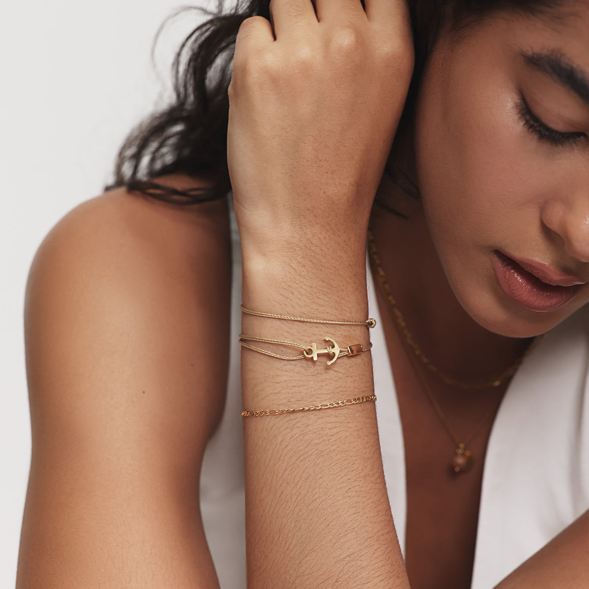 Frau trägt goldenes Unisex Armband mit Gravur & Ankerhaken kombiniert mit feinen Goldketten am Handgelenk