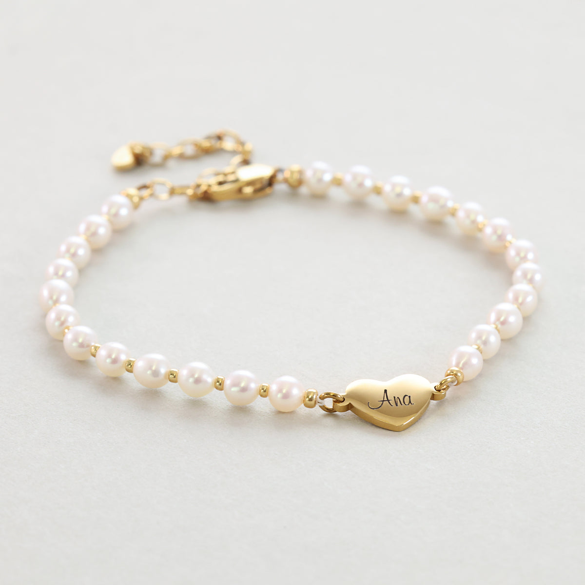 Süßwasser-Perlenarmband mit goldenem Herz-Anhänger und Verlängerungskette, flach liegend fotografiert