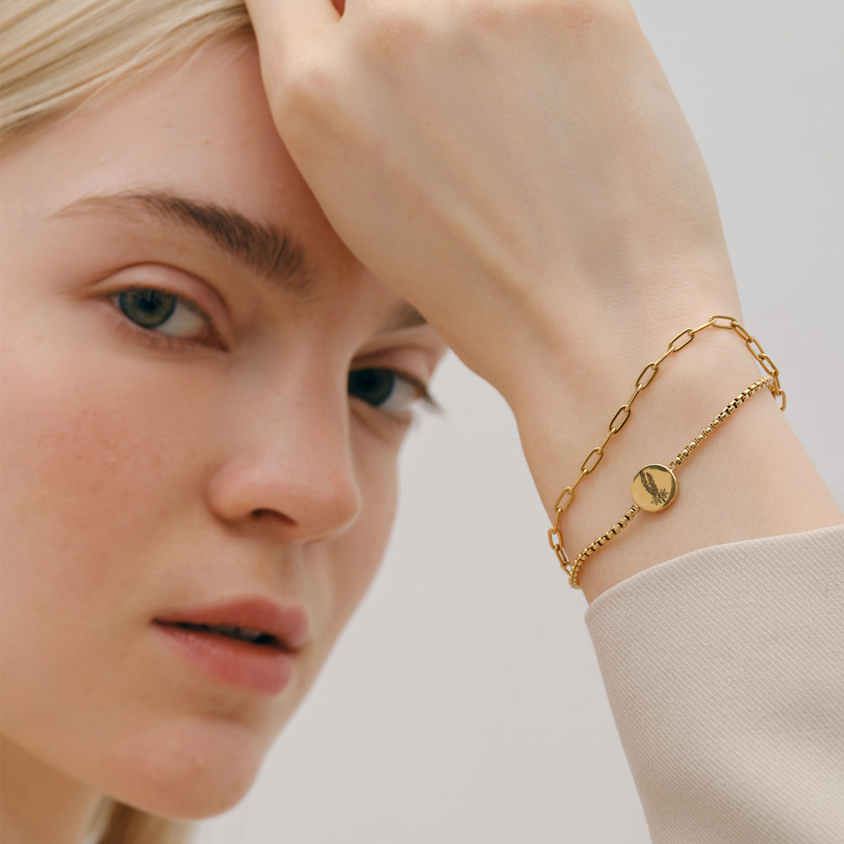 Frau trägt Geburtsblumen-Armband mit rundem Plättchen in Gold, kombiniert mit Kettenarmband