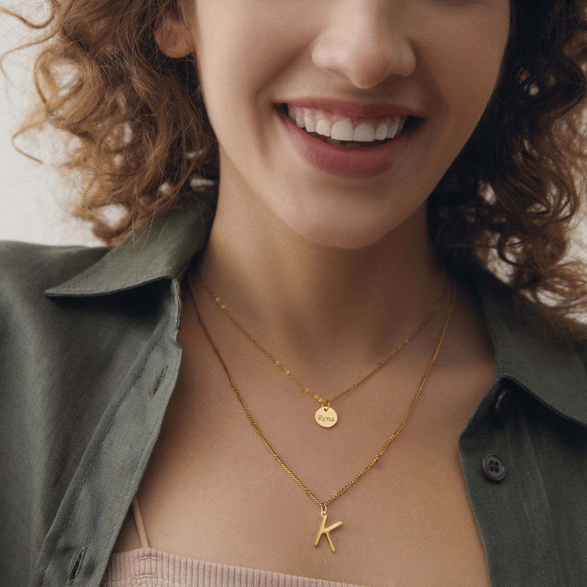 Frau lächelt und trägt goldene Kette mit Buchstaben-Anhänger K