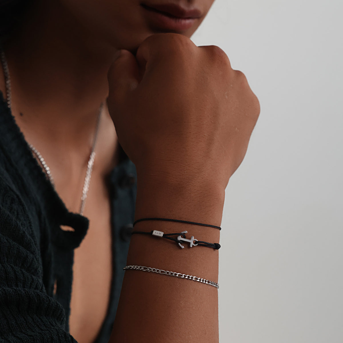 Frau trägt schwarzes Unisex Armband mit Ankerhaken & Gravur kombiniert mit Silberarmband, Hand am Kinn