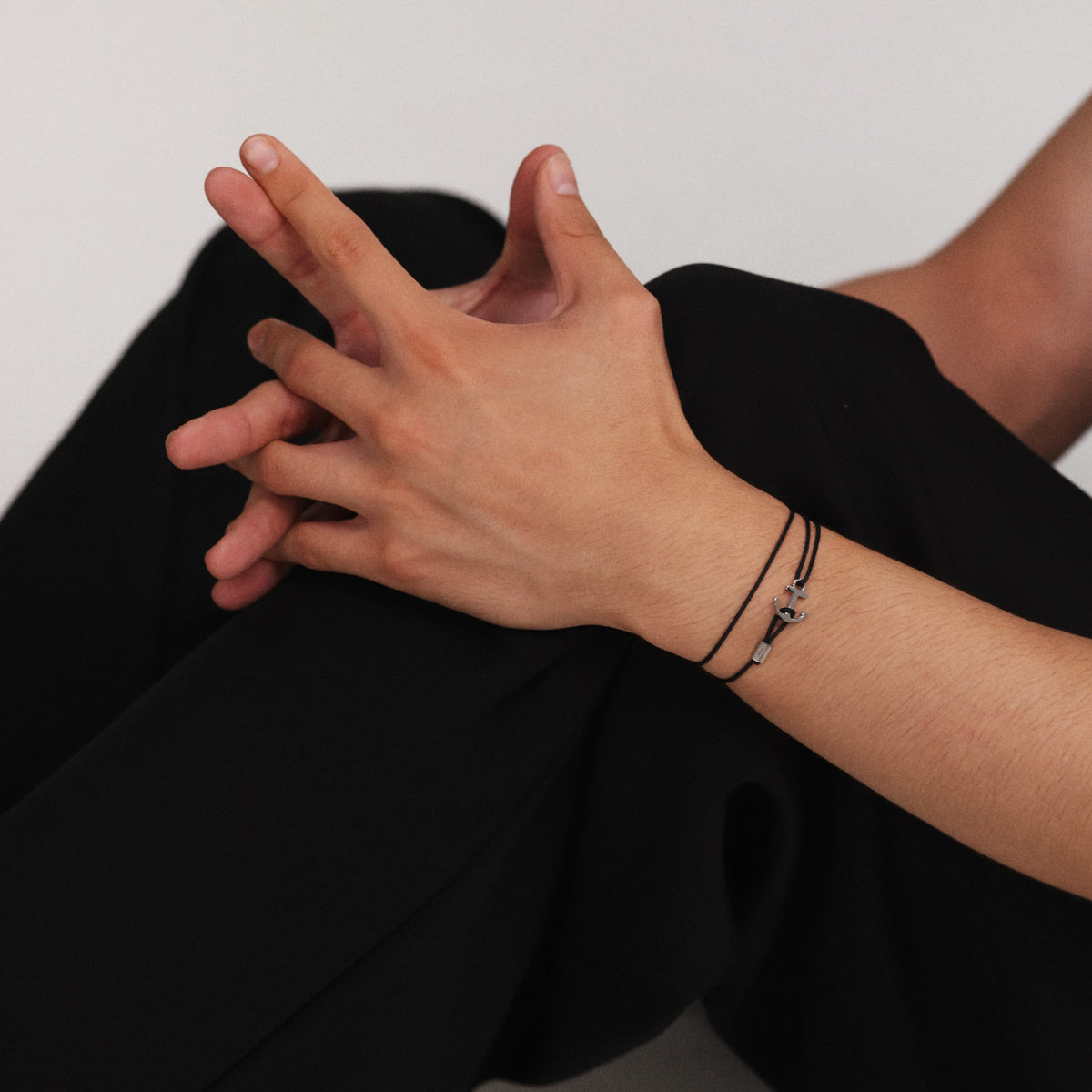 Frau trägt schwarzes Unisex Armband mit Ankerhaken & Gravur am Handgelenk, Beine angewinkelt