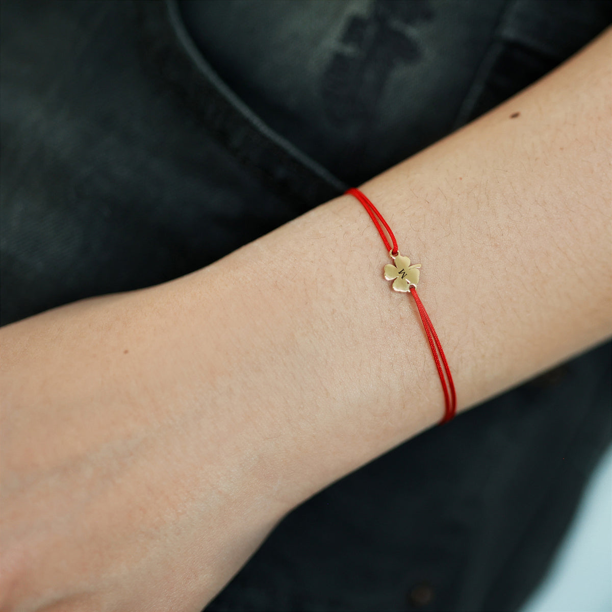 Frau trägt Glücksbringer Armband mit Kleeblatt am Handgelenk, rotes Band mit goldenem Anhänger