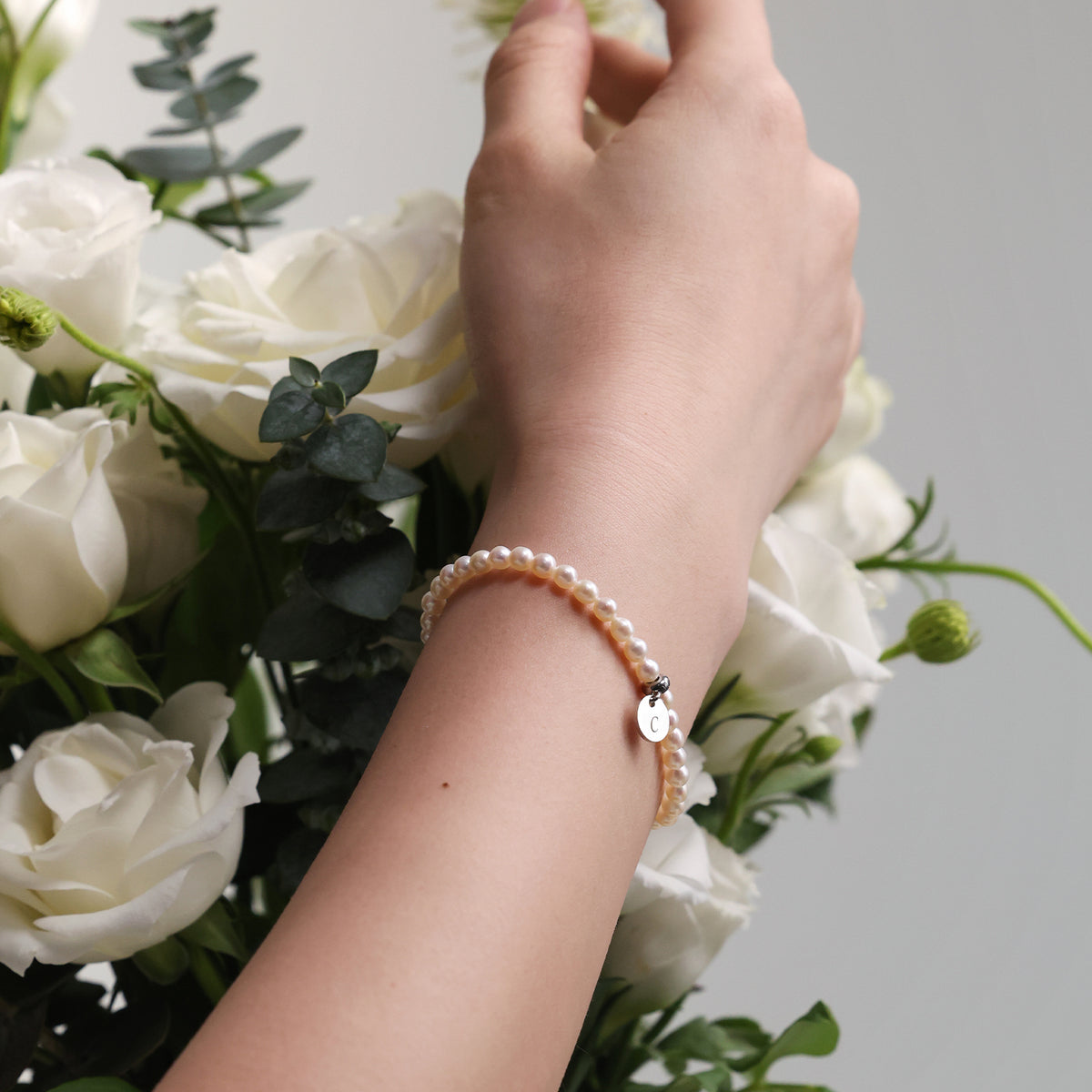 Frau trägt Perlenarmband mit rundem Plättchen am Handgelenk neben weißem Blumenstrauß