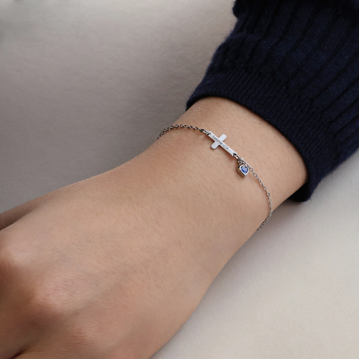 Kreuzarmband mit Herz-Geburtsstein – Frau trägt silbernes Armband mit blauem Herzstein am Handgelenk