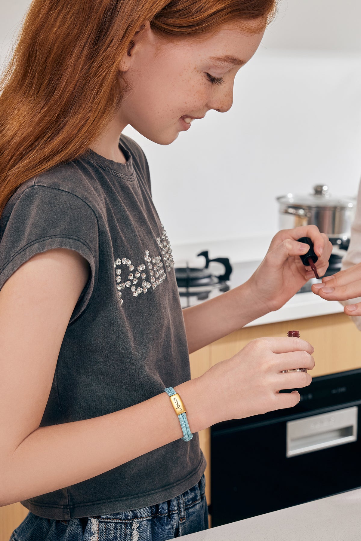 Mädchen trägt hellblaues Glitzer Segeltau Armband mit graviertem Plättchen beim Nagellackieren