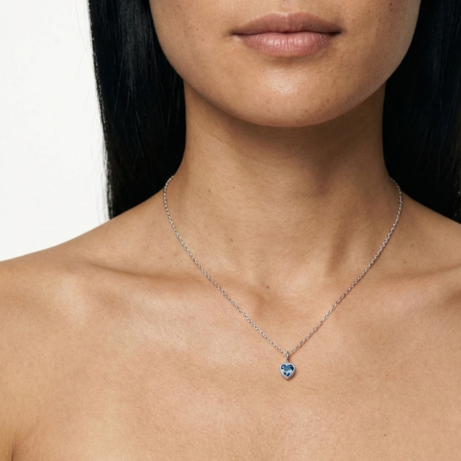 Frau trägt Geburtsstein-Kette in Silber mit herzförmigem blauem Zirkonia-Anhänger am Hals
