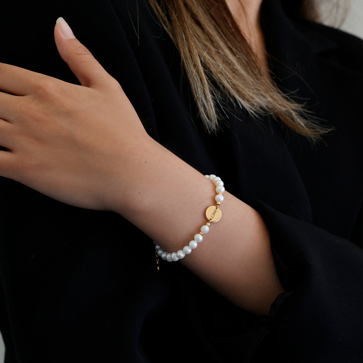 Frau trägt Süßwasserperlen-Armband mit goldenem Gravurplättchen am Handgelenk