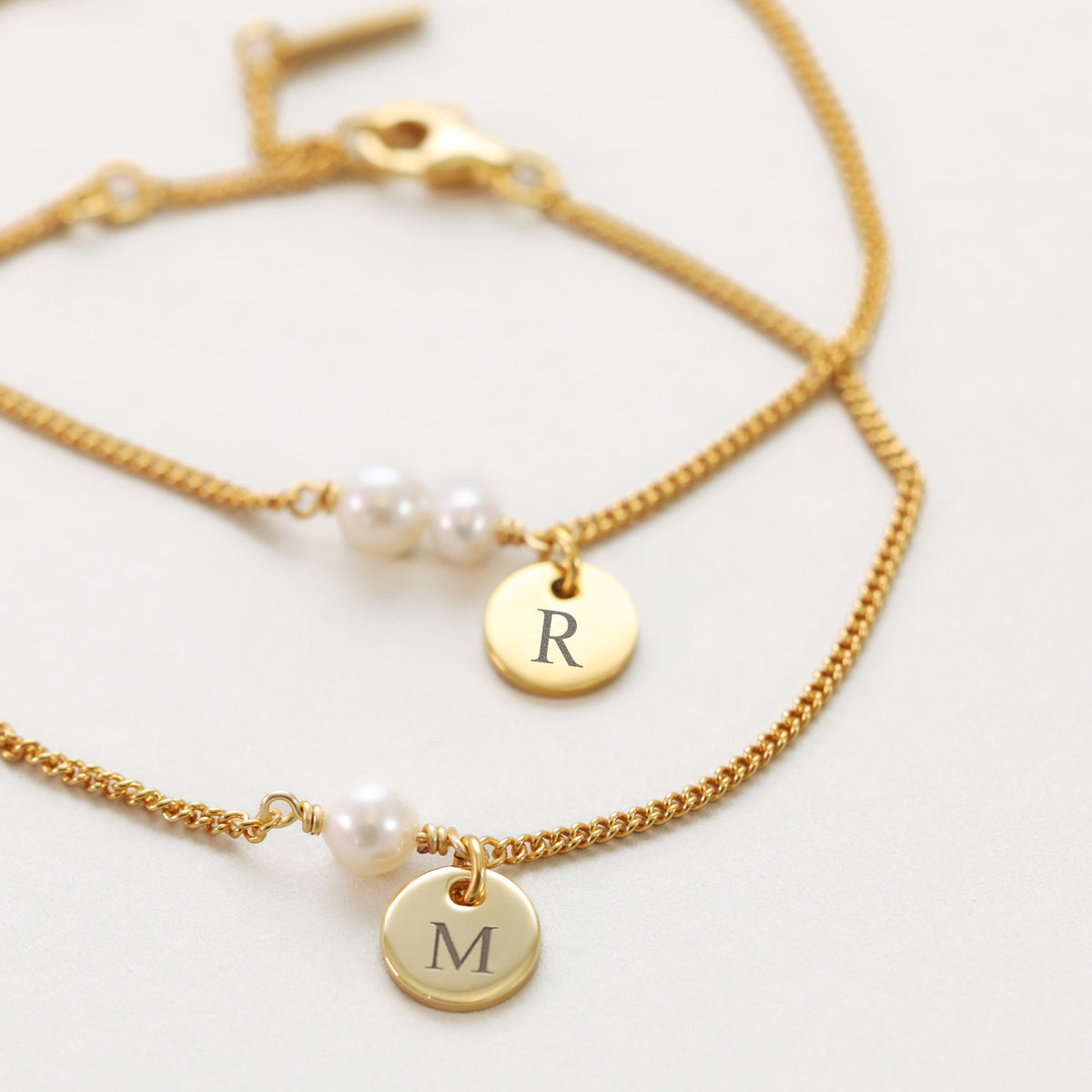 Zwei Armbänder mit Süßwasserperlen und Gravur-Plättchen in Gold, graviert mit Initialen 'R' und 'M'