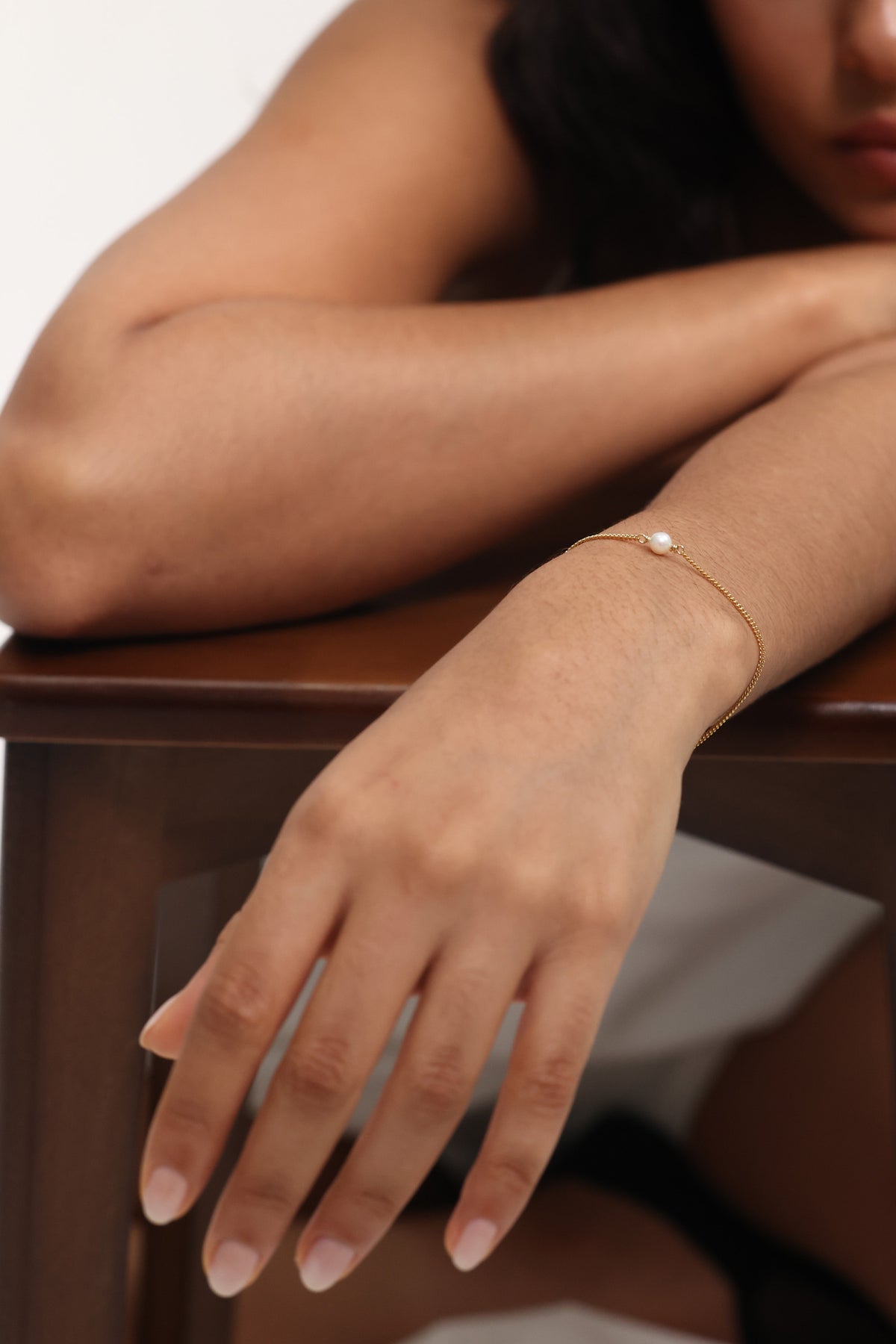 Frau trägt Armband mit Süßwasserperle in Gold, Arm ausgestreckt auf Holztisch