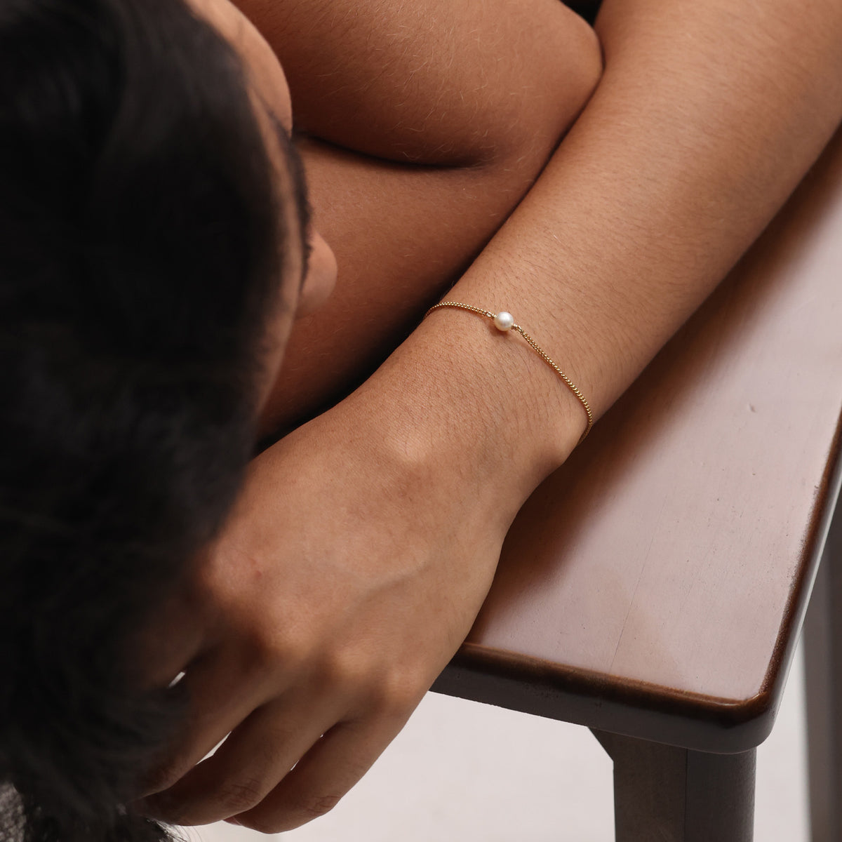 Frau trägt Armband mit Süßwasserperle in Gold am Handgelenk, auf Holztisch abgestützt