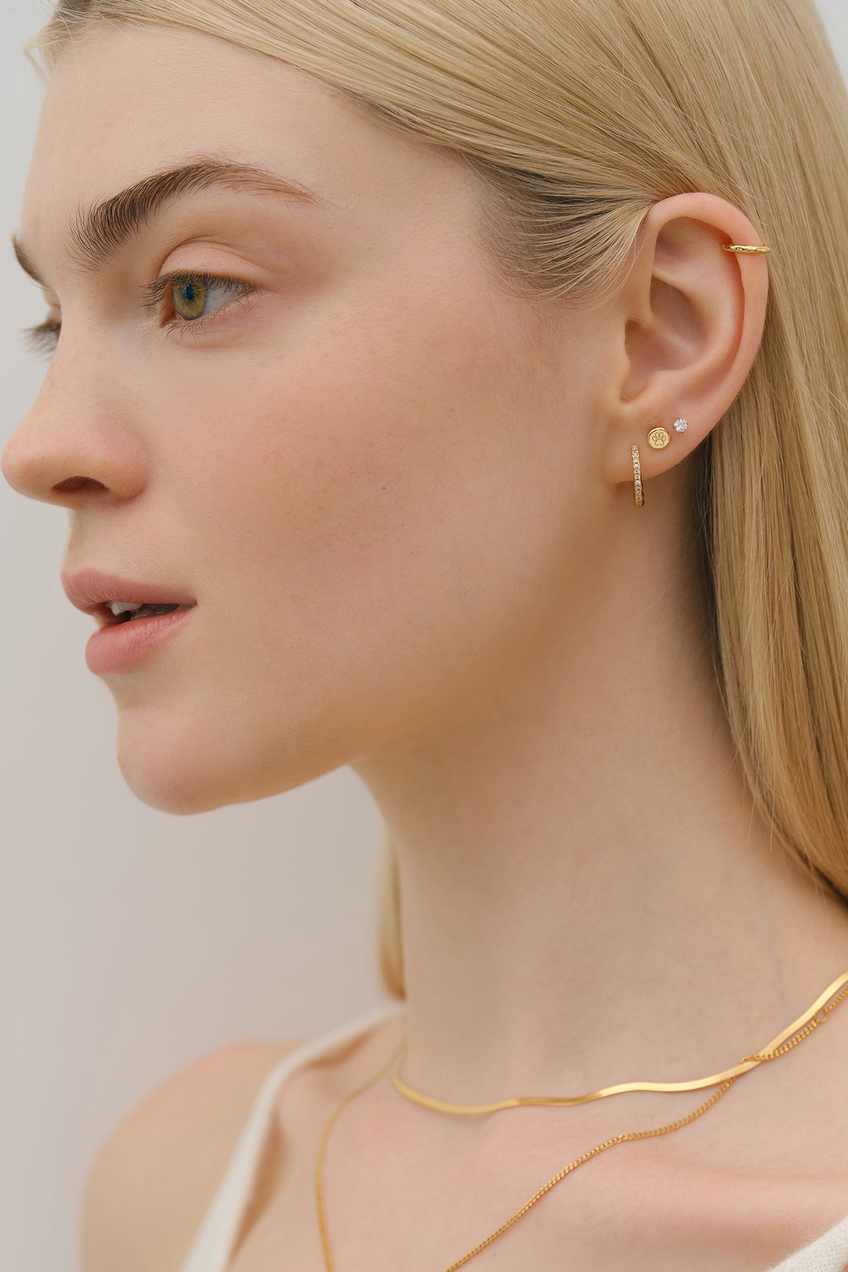 Frau trägt kleine personalisierte runde Ohrstecker in Gold im Ohr-Stack mit Creole und Ear Cuff