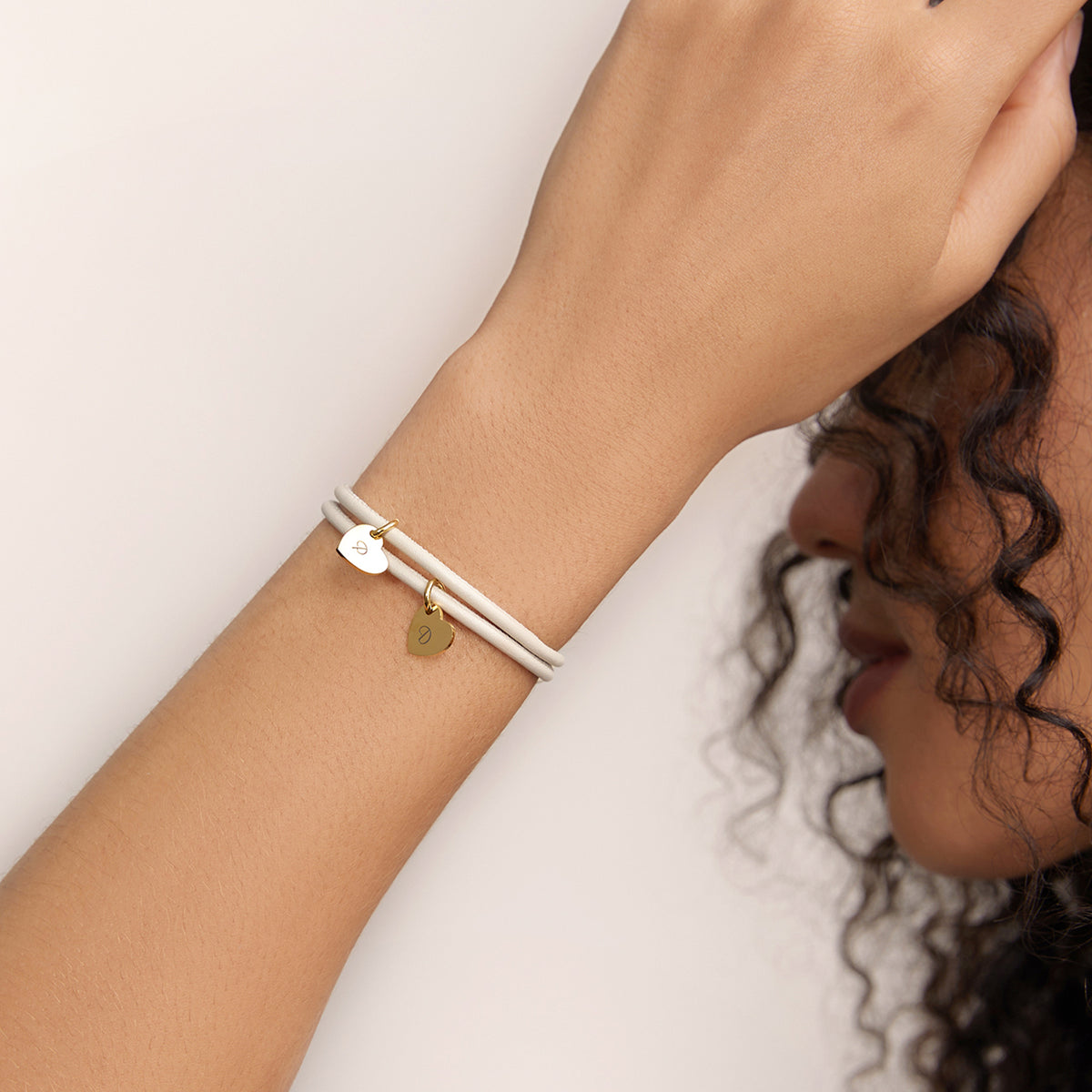 Herz-Anhänger Lederarmband mit Gravur – Frau trägt beiges Armband mit zwei goldenen Herzanhängern