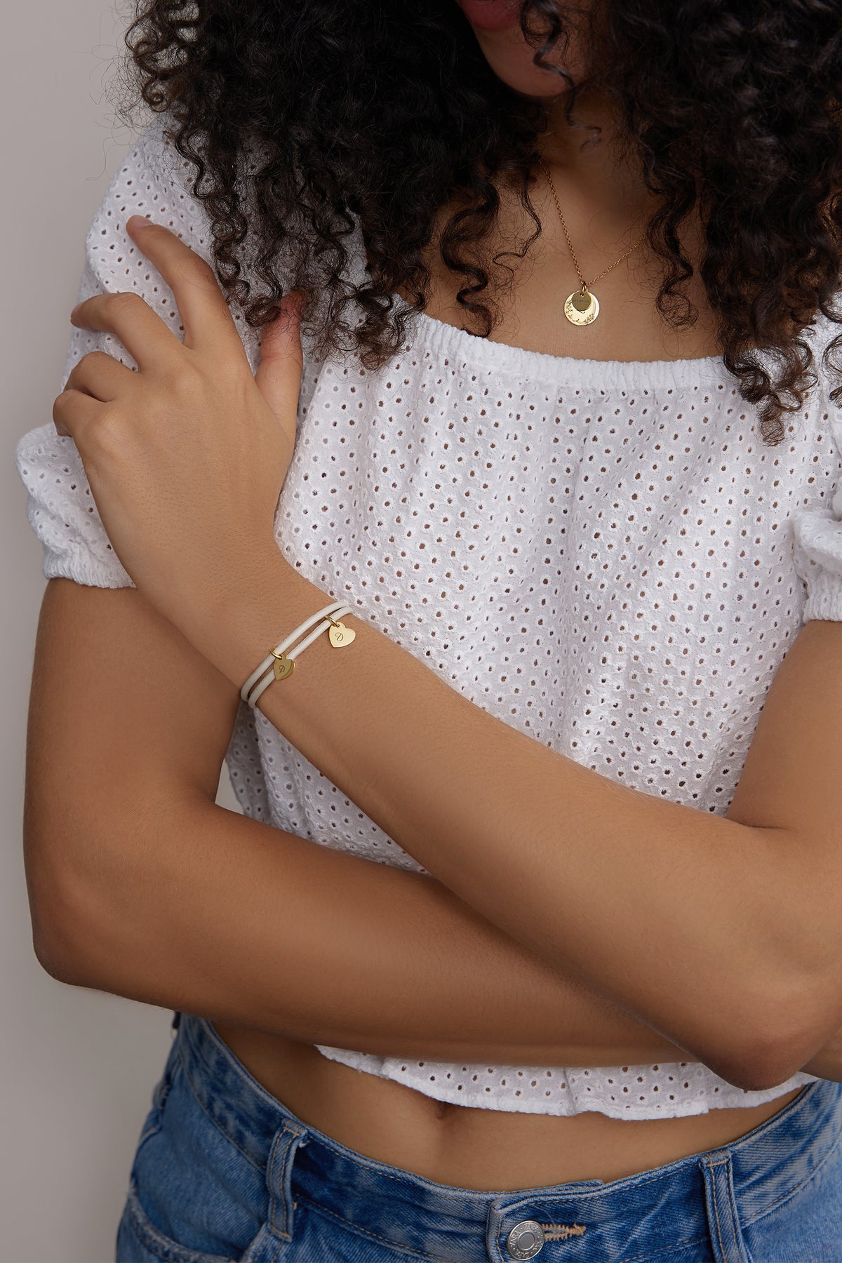 Herz-Anhänger Lederarmband mit Gravur – Frau trägt cremefarbenes Armband mit goldenen Herzanhängern am Arm