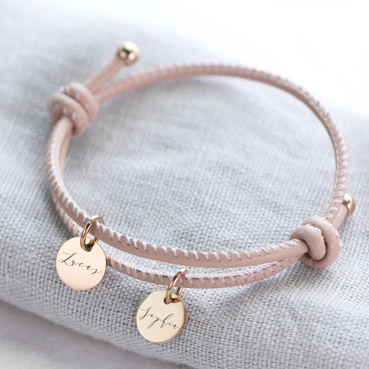 Personalisiertes Lederarmband mit Gravurplättchen in Rosa – zwei goldene Anhänger mit 'Lucas' und 'Sophia'